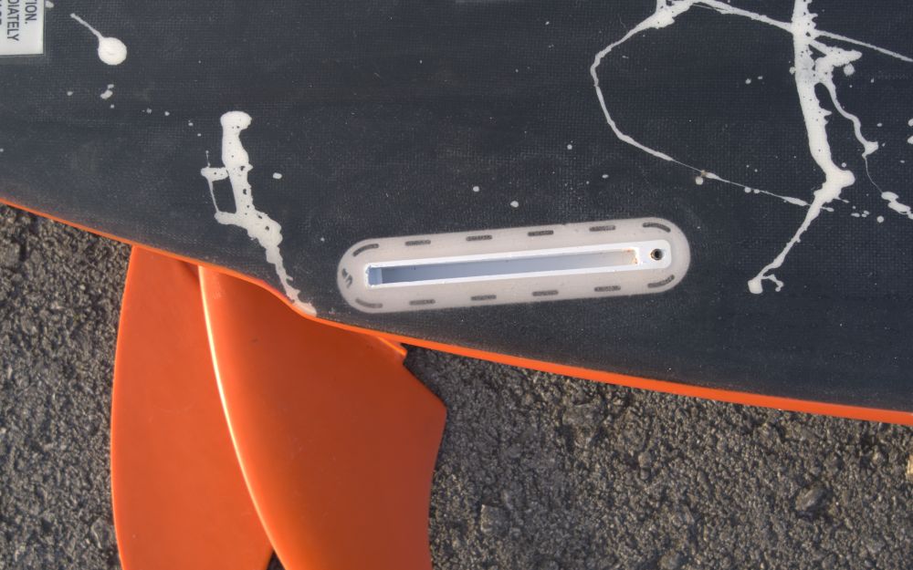 Photo of the underside of a surfboard with a slightly damaged fin plug.